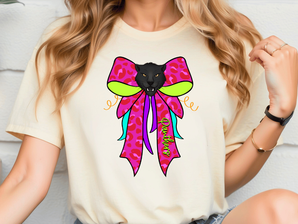A woman wearing a white t-shirt with a colorful graphic design featuring a black panther's face and a pink bow.