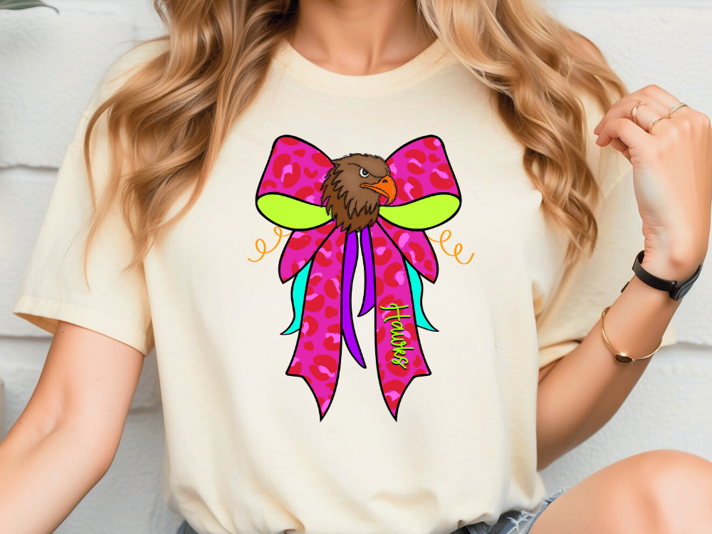 A woman wearing a white t-shirt with a colorful graphic design of a bird's head wearing a pink bow.