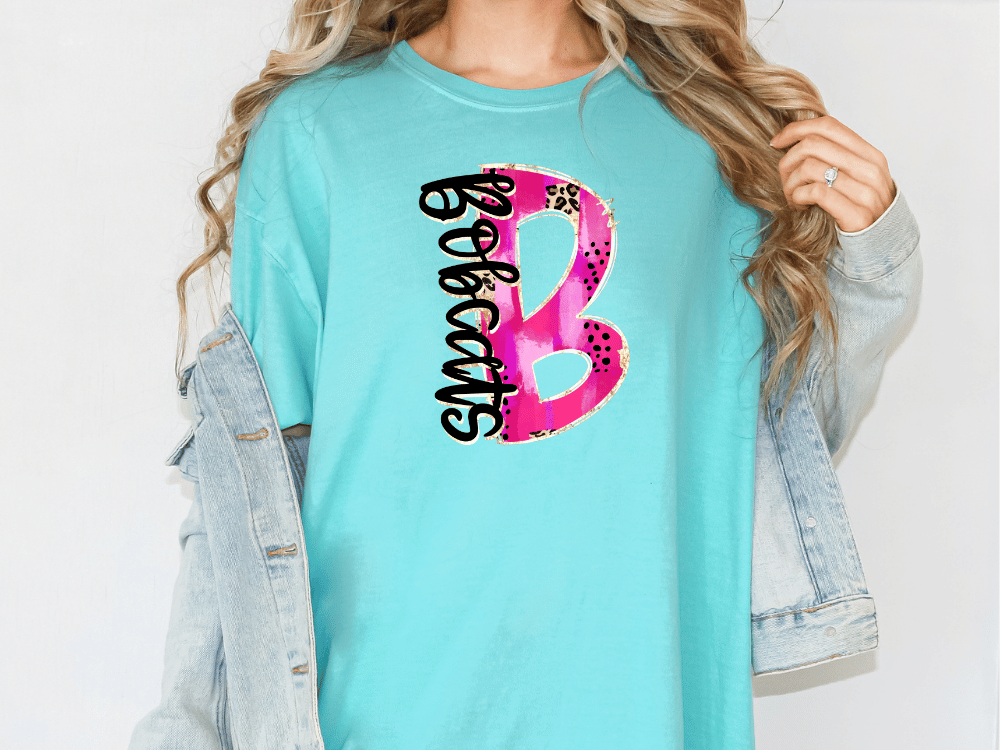 A woman wearing a turquoise t-shirt with a graphic design and a denim jacket.