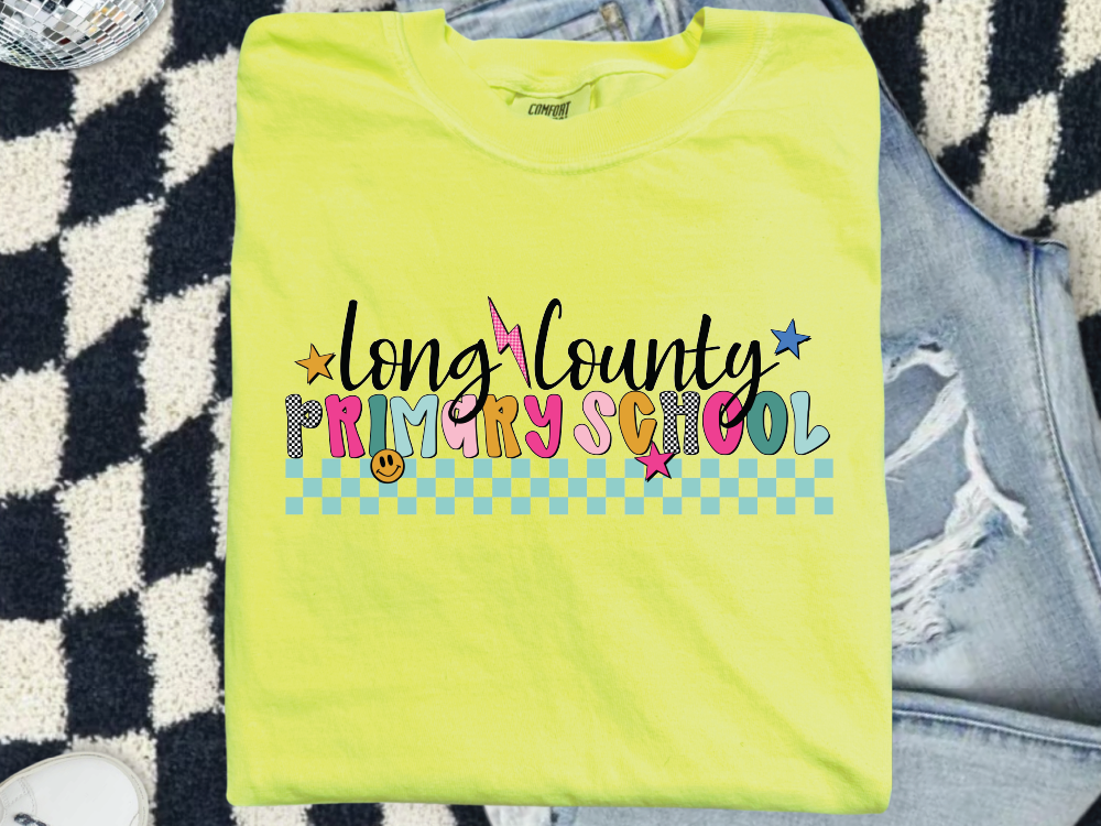 A bright yellow t-shirt with colorful text and graphics, including the words "Long County Primary School" and various decorative elements, is displayed on a patterned surface.