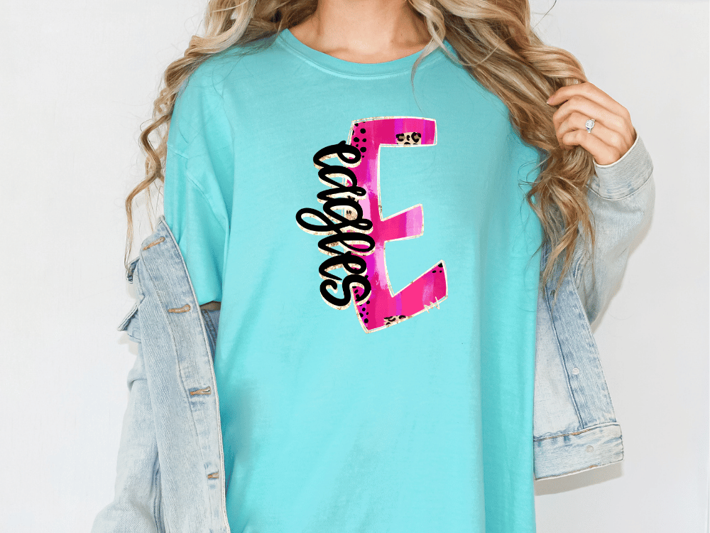 A person wearing a turquoise t-shirt with a pink and black graphic design on it, along with a denim jacket.