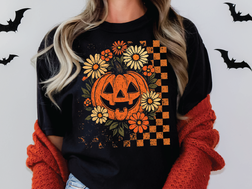 A woman wearing a black t-shirt with a pumpkin and flower design, along with a red sweater, stands against a white background with bats.