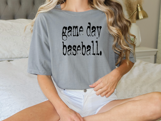 a woman sitting on a bed wearing a game day baseball shirt