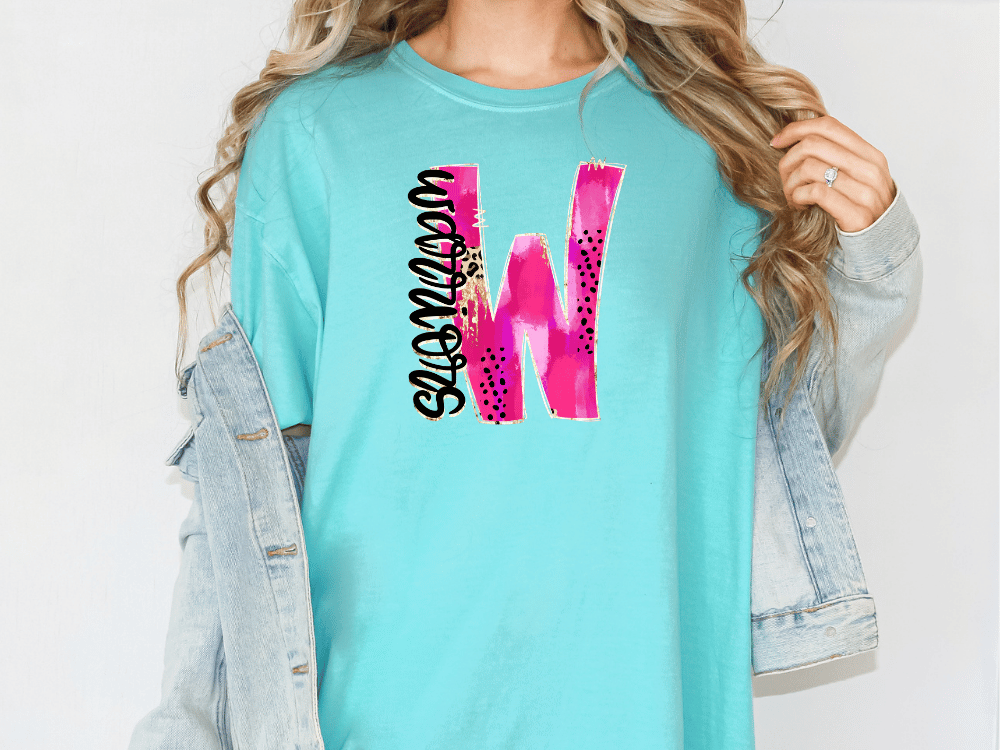 A woman wearing a turquoise t-shirt with a pink and black graphic design on it, and a denim jacket.