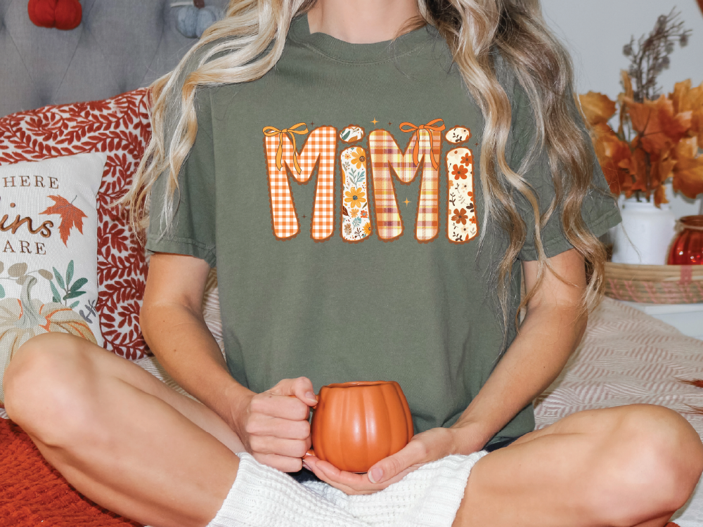 A person sitting on a bed with a pumpkin-themed t-shirt and holding a pumpkin-shaped mug.