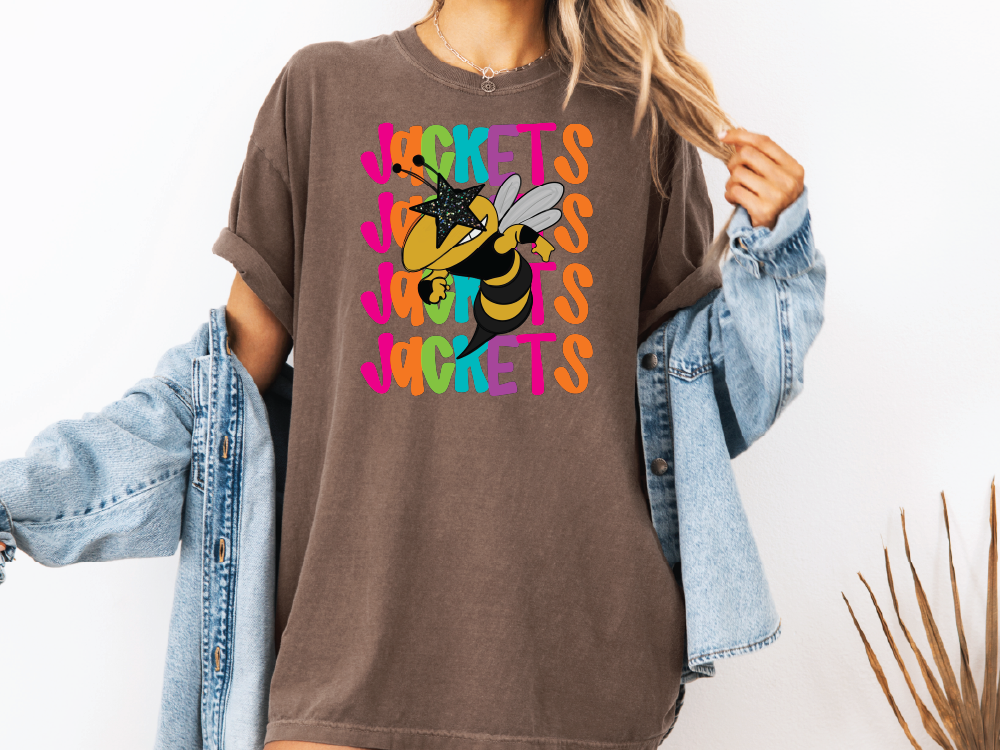 A woman wearing a brown t-shirt with a graphic of a bee and the word "JACKETS" printed on it, along with a denim jacket.