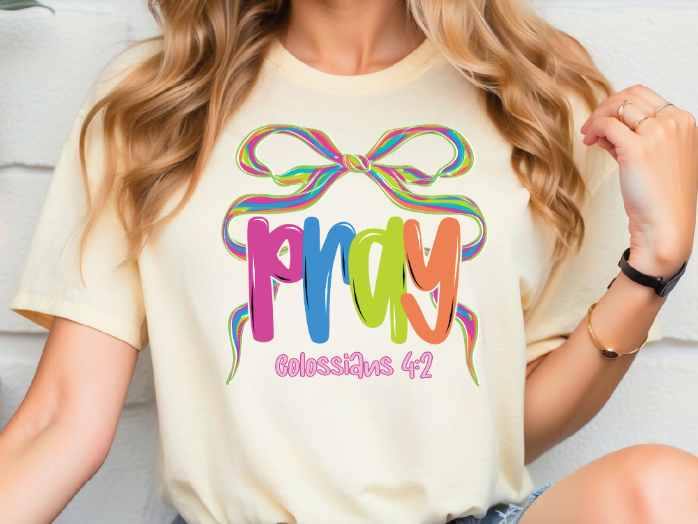 A woman wearing a white t-shirt with a colorful graphic design that says "Pray" and "Colossians 4:2".