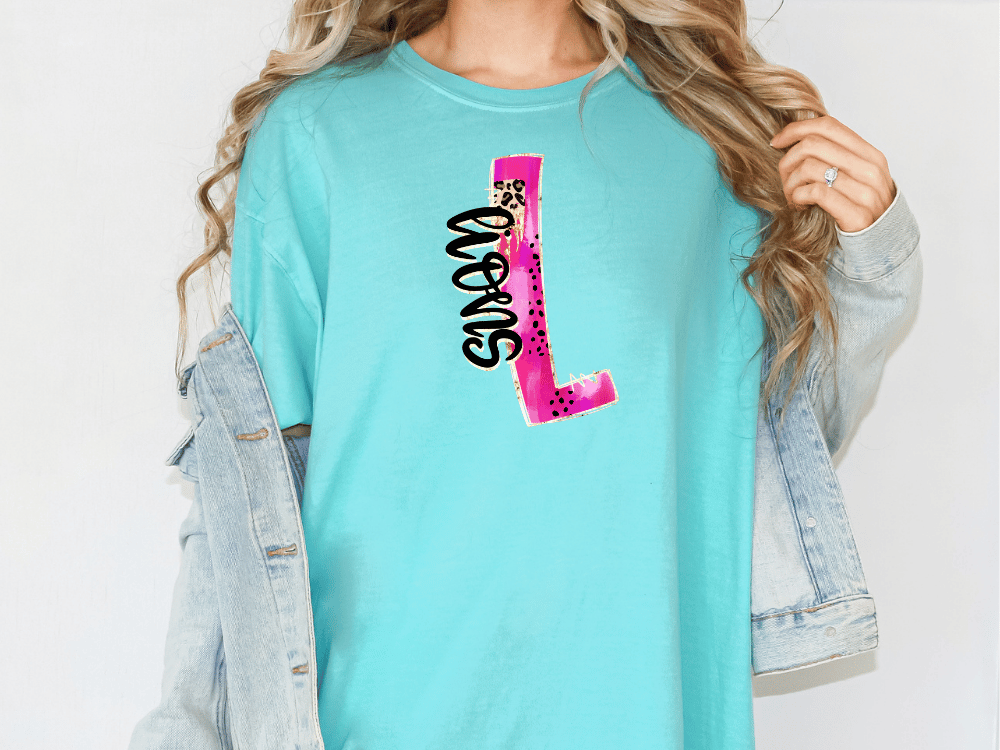A woman wearing a turquoise t-shirt with a pink and black design on it, and a denim jacket.