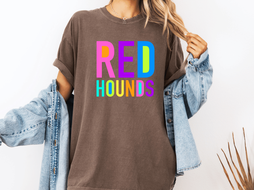 A person wearing a brown t-shirt with the text "RED HOUNDS" in colorful letters, along with a denim jacket, stands against a white background.