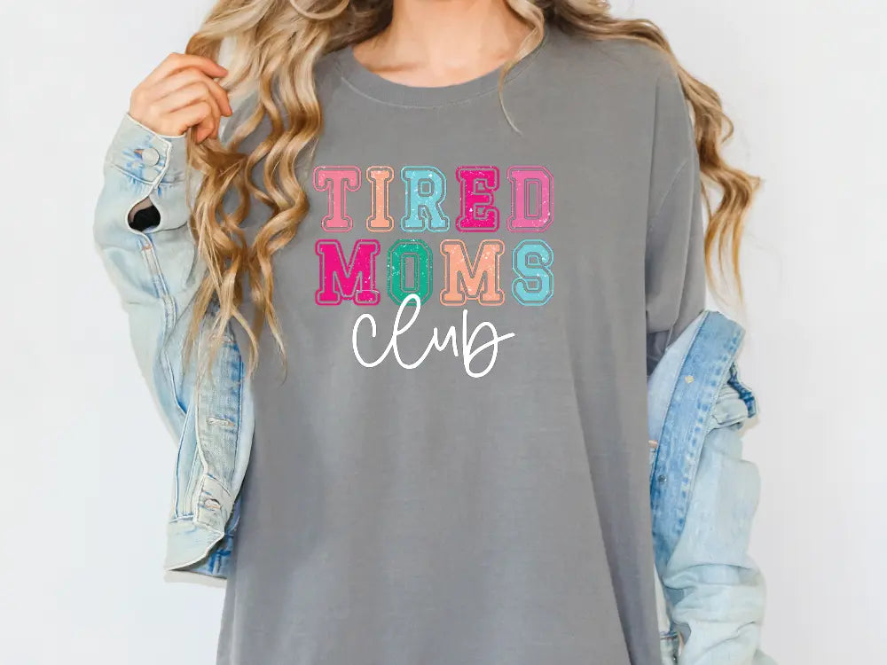 a woman wearing a grey shirt that says tired moms club