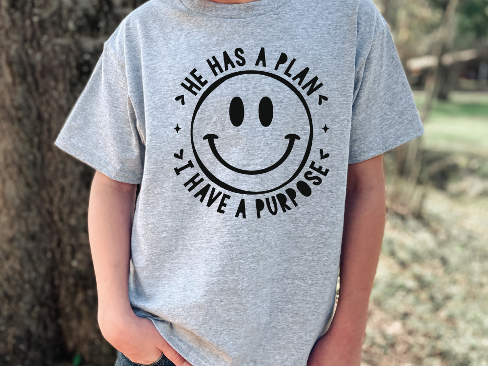 A person wearing a gray t-shirt with a black smiley face design and text around it.