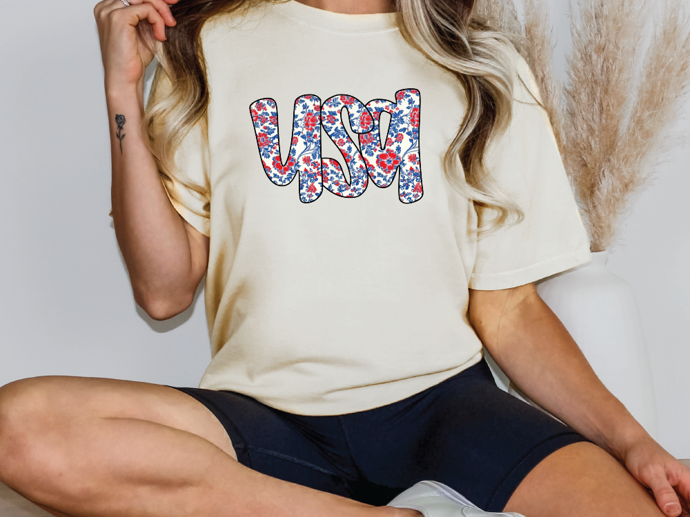 a woman sitting on a bed wearing a t - shirt with the word usa printed