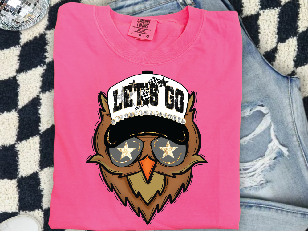A pink t-shirt with a graphic design of an owl wearing sunglasses and a hat with the text "LET'S GO" printed on it.