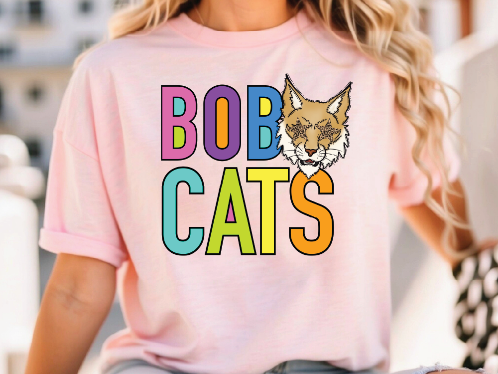 A woman wearing a pink t-shirt with the text "BOBCATS" printed on it, along with a cartoon image of a bobcat.