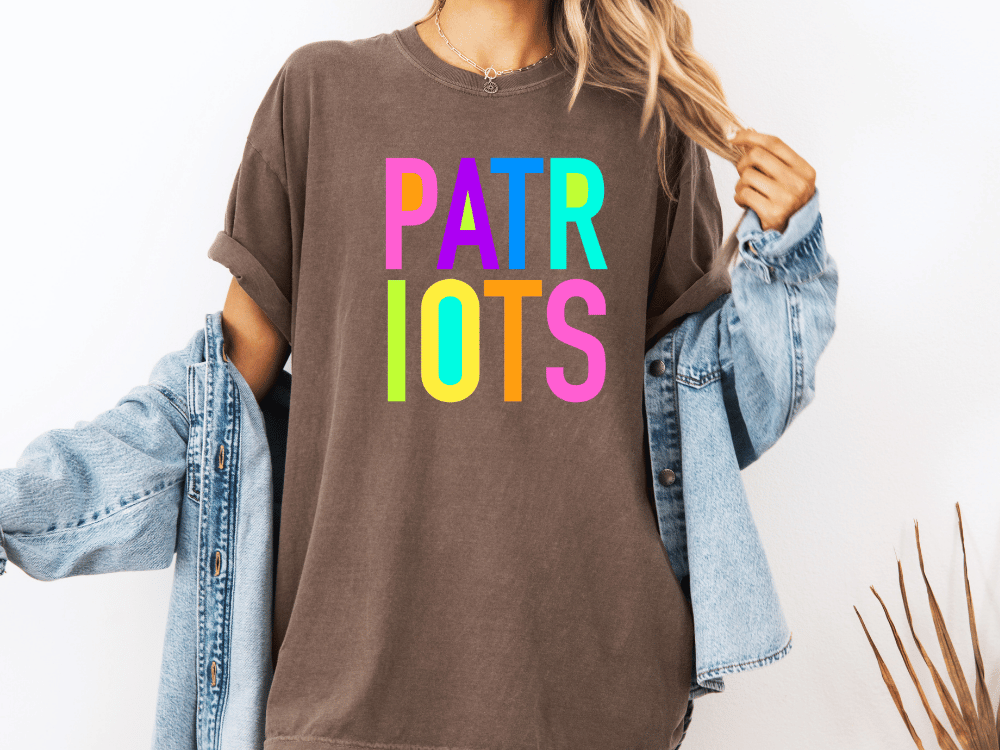 A person wearing a brown t-shirt with the text "PATRIOTS" in colorful letters, paired with a denim jacket, stands against a white background.