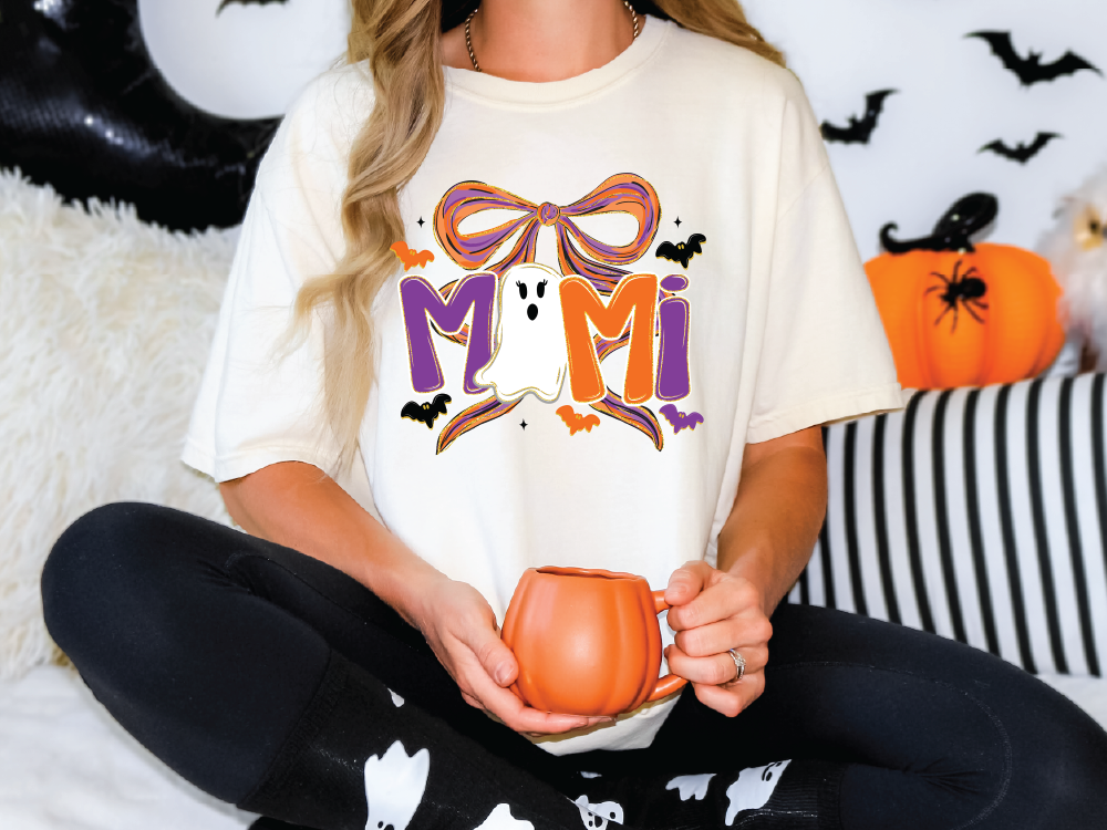 A woman wearing a white t-shirt with a graphic design of a ghost and a pumpkin, holding a mug in her hands.