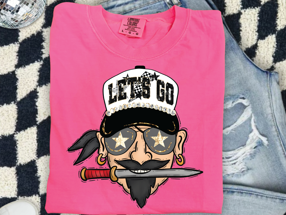 A pink t-shirt with a cartoon pirate face and a pirate hat, along with a pair of jeans and a checkered patterned rug.