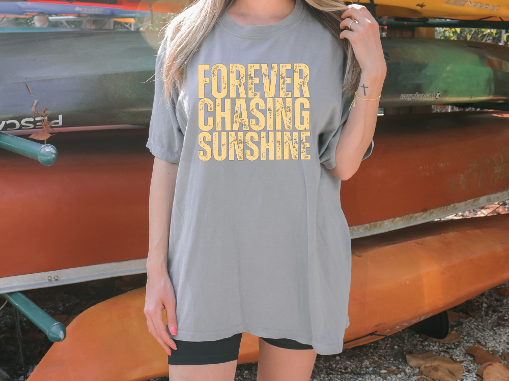 a woman standing in front of a boat wearing a shirt that says forever chasing sunshine