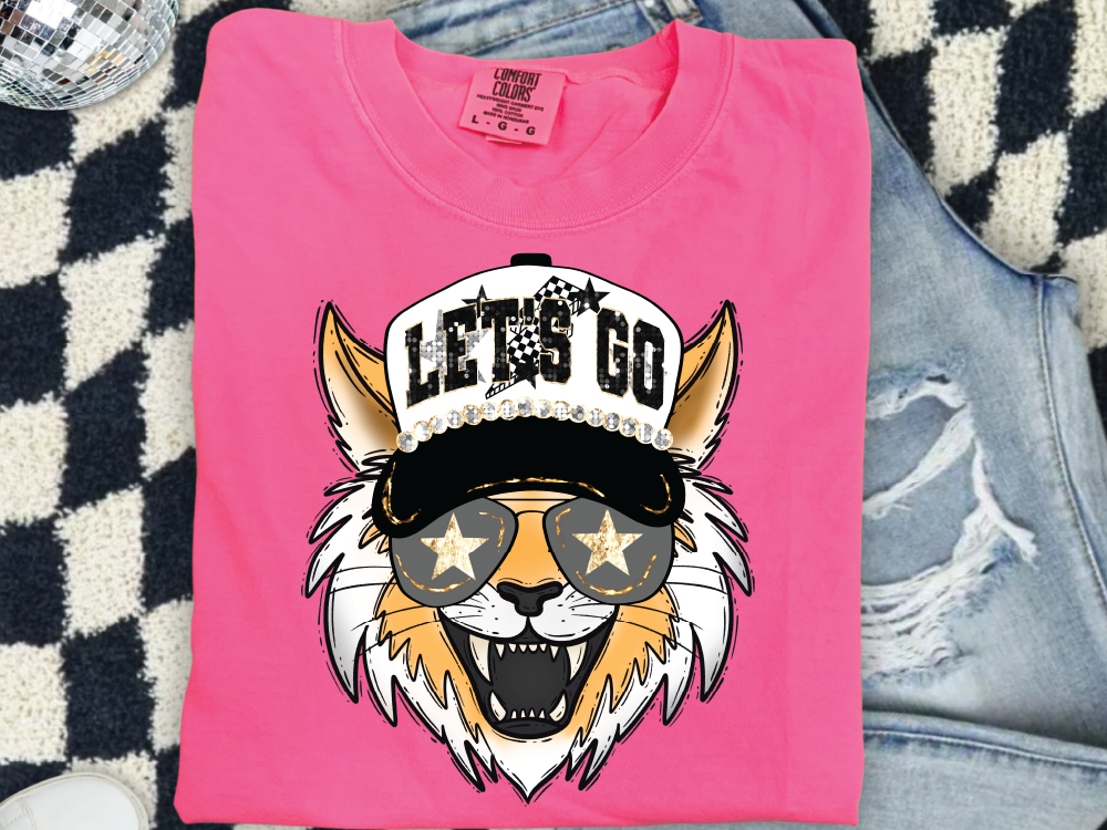 A pink t-shirt with a graphic design of a cat wearing sunglasses and a baseball cap with the text "LET'S GO" printed on it.