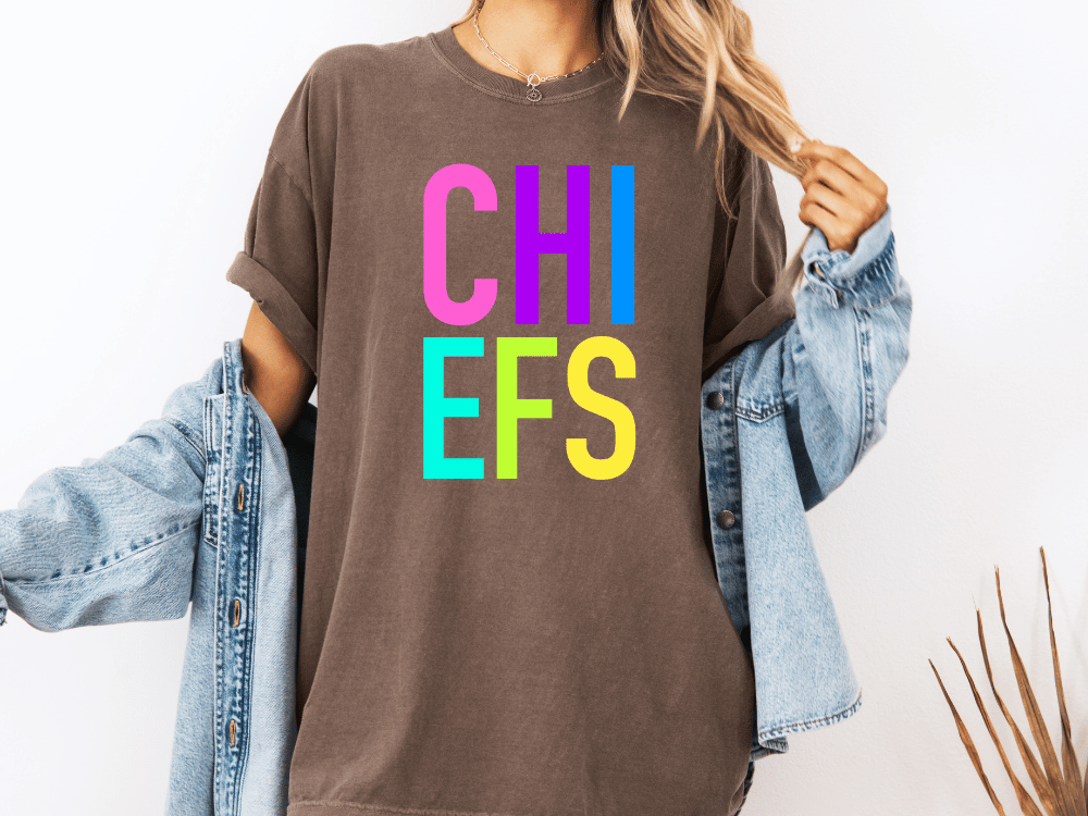 A person wearing a brown t-shirt with the text "CHI EFS" in colorful letters, along with a denim jacket, stands against a white background.