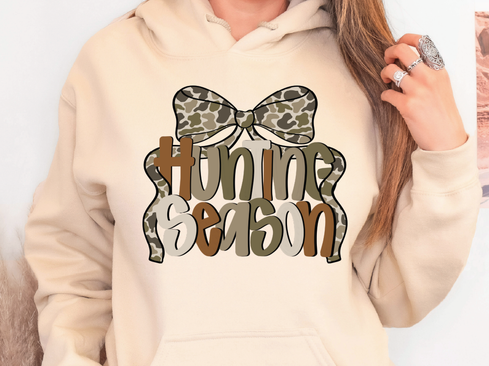 A person wearing a beige hoodie with a graphic design that says "Hunting Season" on it.