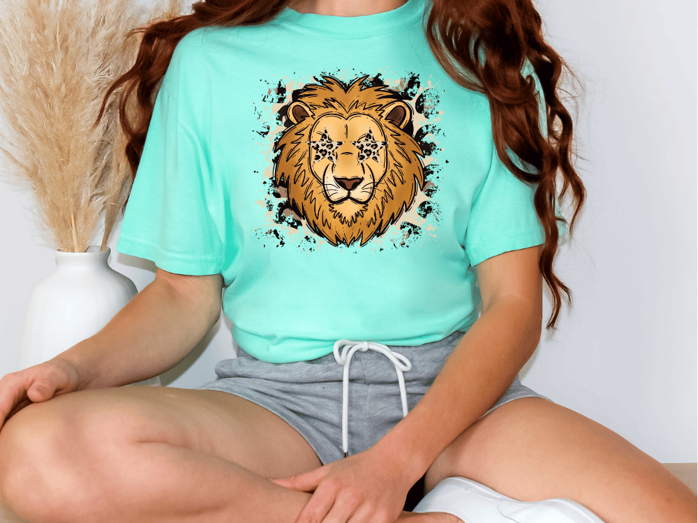 A person wearing a turquoise t-shirt with a lion graphic and gray shorts is sitting on the floor.