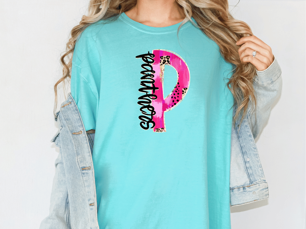 A woman wearing a turquoise t-shirt with a pink and black design on it, and a denim jacket.