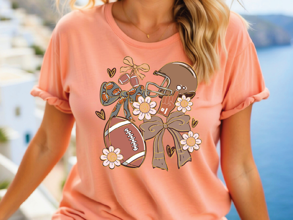 A woman wearing a peach-colored t-shirt with a graphic design featuring a football, flowers, and a bow.