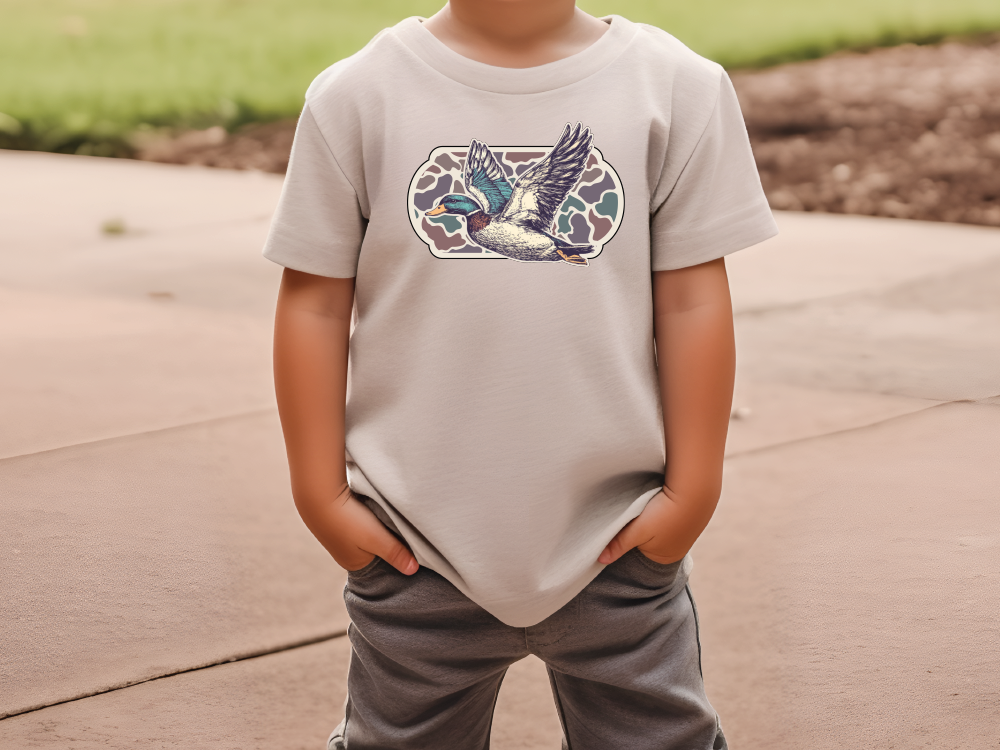 a young boy standing on a sidewalk wearing a t - shirt with a bird on