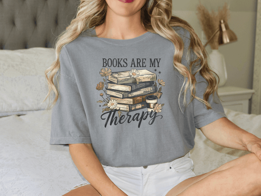 A woman wearing a gray t-shirt with a graphic design of books and flowers, along with the text "Books are my therapy".