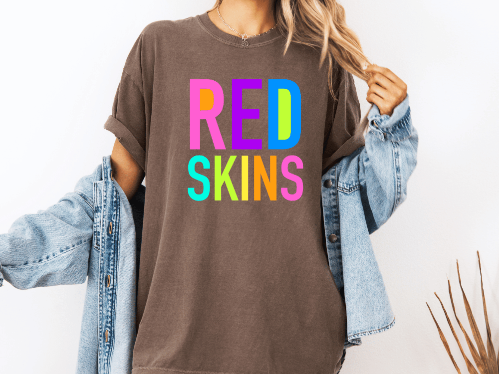 A person wearing a brown t-shirt with the text "RED SKINS" in colorful letters, along with a denim jacket, stands against a white background.