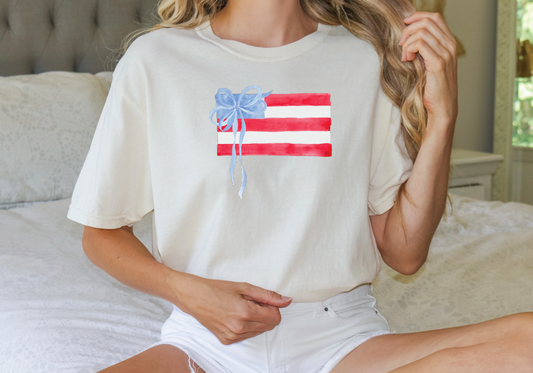 a woman sitting on a bed holding a t - shirt with an american flag on