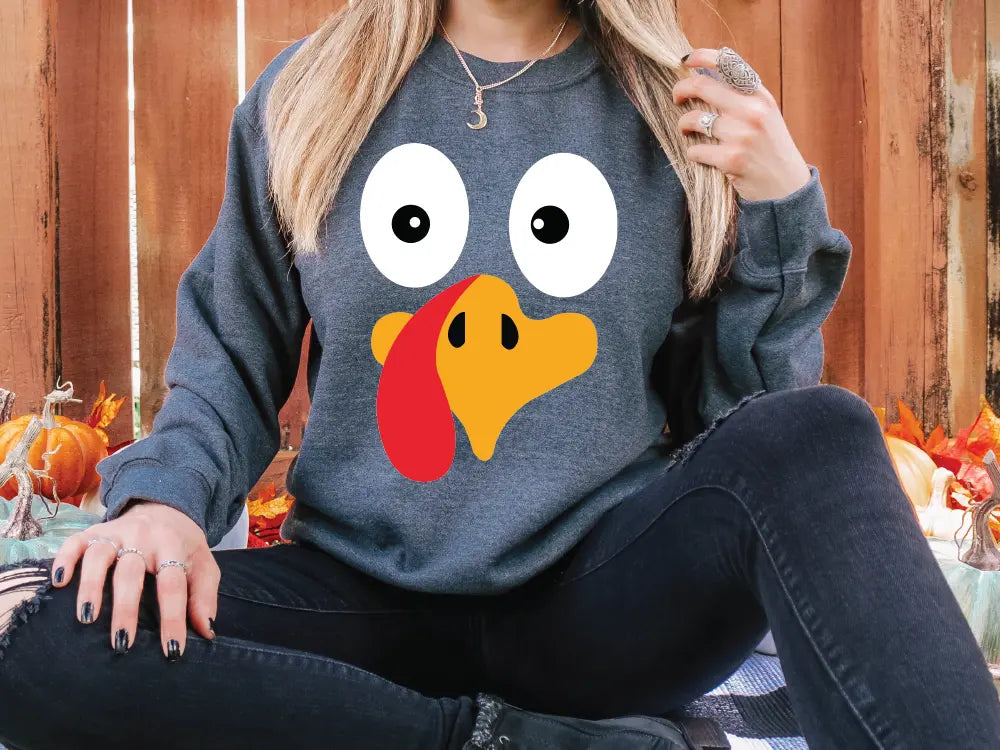 a woman sitting on the ground wearing a sweatshirt with a turkey face on it