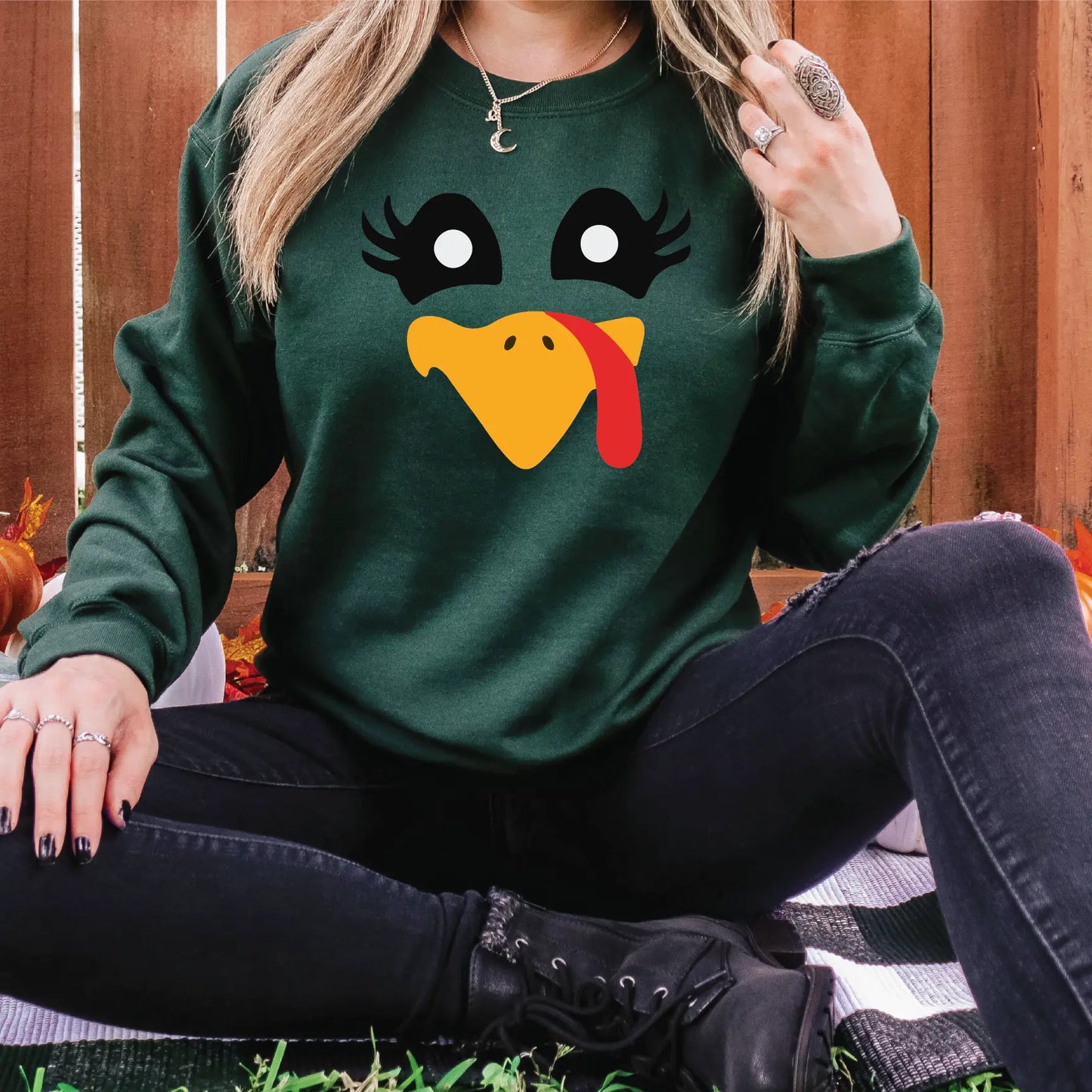 a woman sitting on the ground wearing a green sweatshirt with a turkey face on it