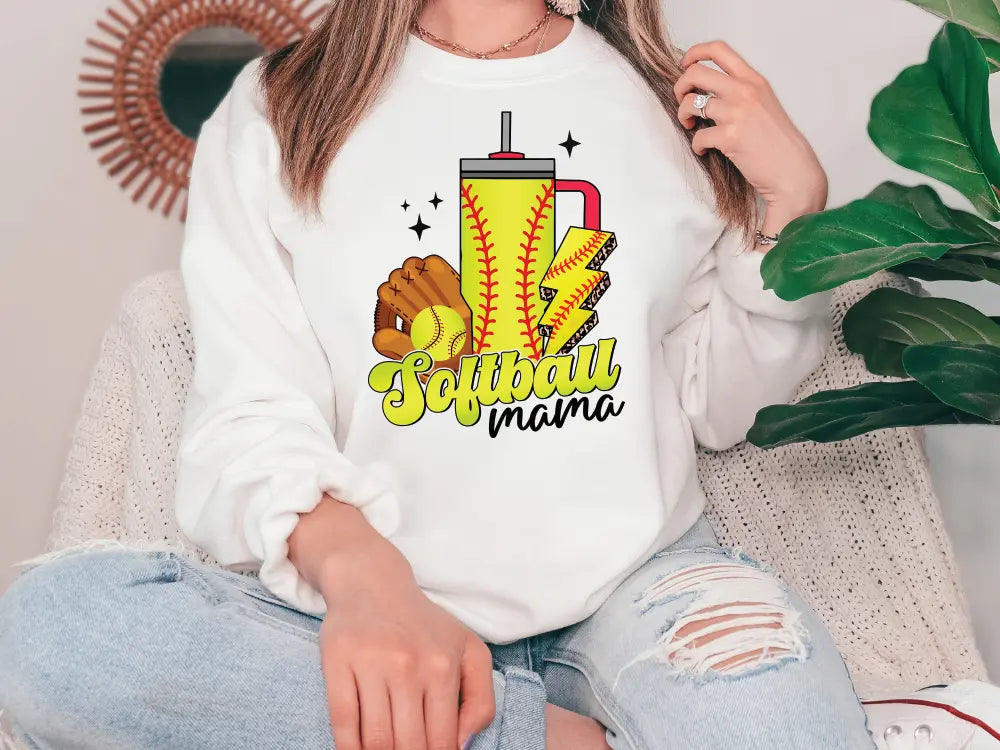 a woman sitting on a couch wearing a softball mom sweatshirt