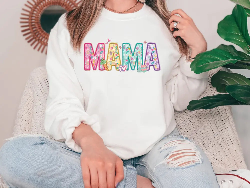 a woman sitting on a couch wearing a white sweatshirt with the word mama printed on