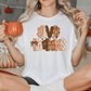 A woman sitting on a bed, holding a mug and wearing a white t-shirt with a Thanksgiving-themed graphic.