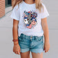 a little girl standing on a sidewalk wearing a t - shirt with a picture of