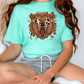 A person wearing a turquoise t-shirt with a graphic of a brown bear and a red mouth, sitting cross-legged on the floor.