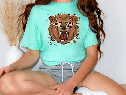 A person wearing a turquoise t-shirt with a graphic of a brown bear and a red mouth, sitting cross-legged on the floor.