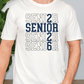A white t-shirt with the text "SENIOR SENIOR SENIOR SENIOR SENIOR" printed on it in blue and white.