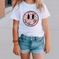 a little girl wearing a white shirt with a smiley face on it