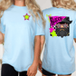 two women wearing light blue t-shirts with colorful designs on the back.
