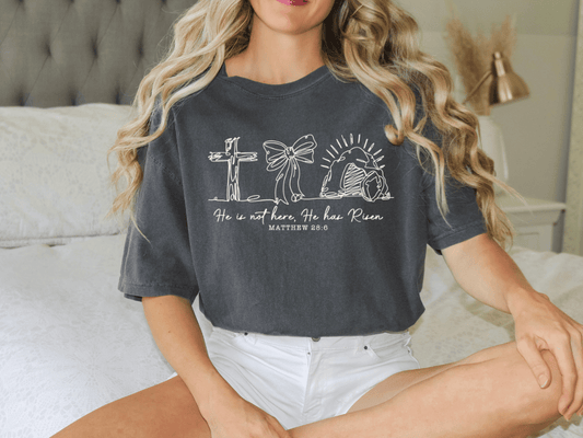 A woman wearing a gray t-shirt with a graphic design and text printed on it, sitting on a bed.