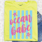 A yellow t-shirt with the text "ocean babe" printed on it, along with pink and blue striped designs.