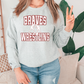 A woman wearing a grey sweatshirt with the text "Braves Wrestling" printed on it, standing in front of a plant.