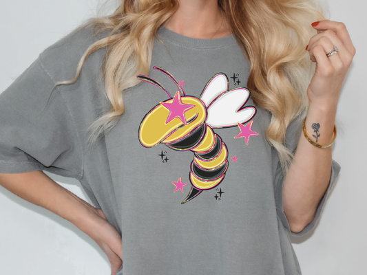 A woman wearing a gray t-shirt with a colorful graphic of a bee and stars on it.