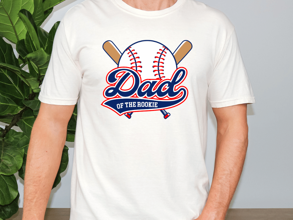 A white t-shirt with a graphic design featuring a baseball and the text "DAD of the ROOKIE" printed on it.