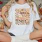 A woman wearing a white t-shirt with a pumpkin patch design and the text "Take me to the pumpkin patch" is sitting on a bed with a pillow featuring a pumpkin and fall-themed design.