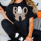 A person wearing a black t-shirt with a graphic of a ghost and a bow, sitting on a couch with Halloween decorations in the background.
